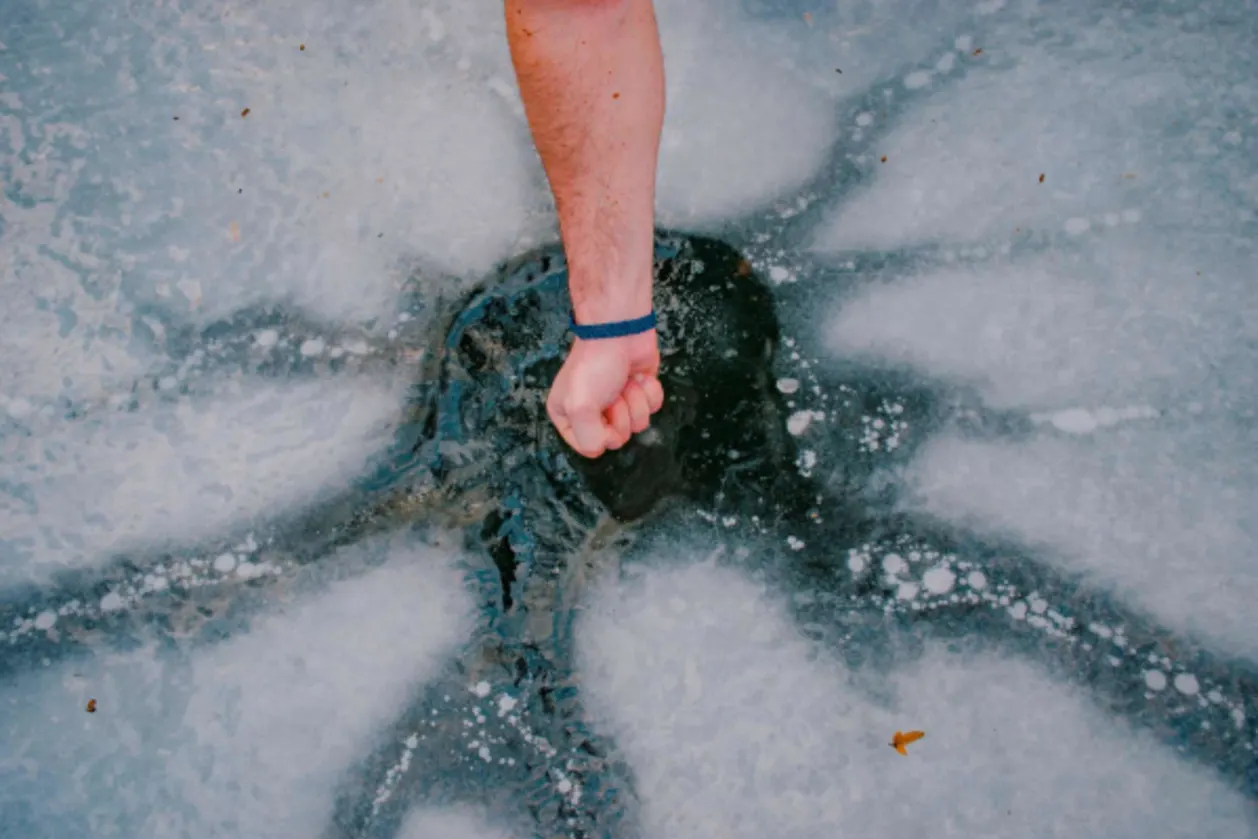 man's hand cracking ice in lake